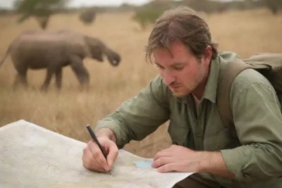 Viajero examinando un mapa de safari con animales salvajes en el fondo.