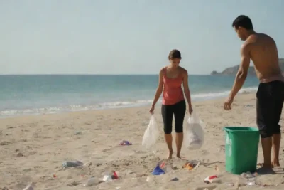 Voluntarios coleccionando basura en una playa con el océano en el fondo.