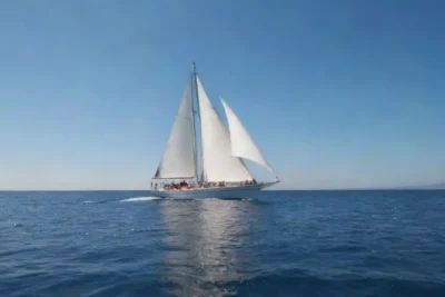 Velero navegando en aguas abiertas bajo un claro cielo azul con la tripulación disfrutando del viaje.
