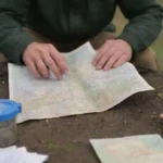 Person revisa un mapa y empaca suministros de emergencia mientras se encuentra en un entorno rural.